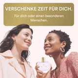 Two women holding a perfume bottle with a promotional message in German.