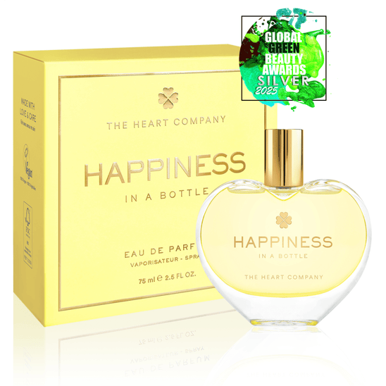 Happiness in a Bottle perfume by The Heart Company in a heart-shaped glass bottle with gold cap, shown with yellow packaging and Global Green Beauty Awards Silver 2025 badge, representing joyful, uplifting fragrance and clean beauty
