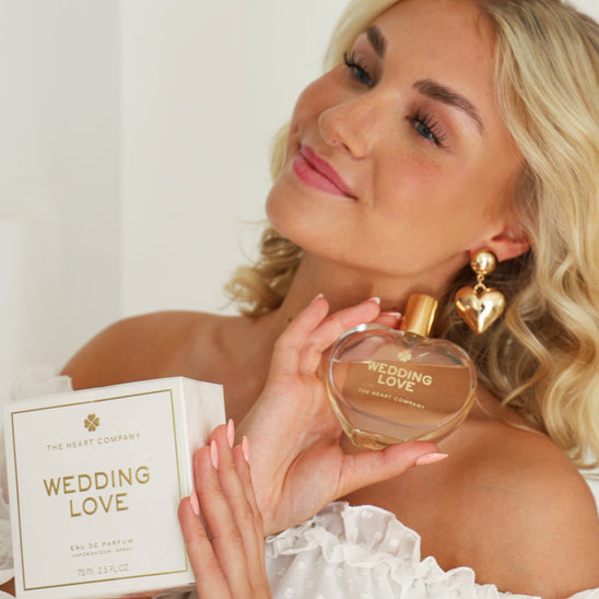 Bride holding Wedding Love perfume in heart-shaped bottle and gift box, wearing white dress and showcasing romantic bridal fragrance.
